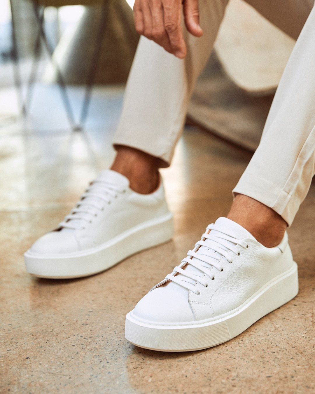 White leather minimal sneakers with thick soles paired with light beige trousers.
