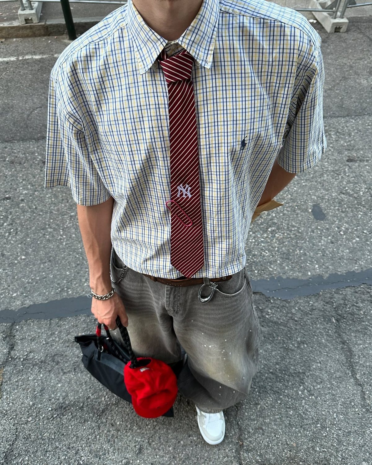 Man wearing a short-sleeved plaid shirt, red striped tie, and grey trousers.