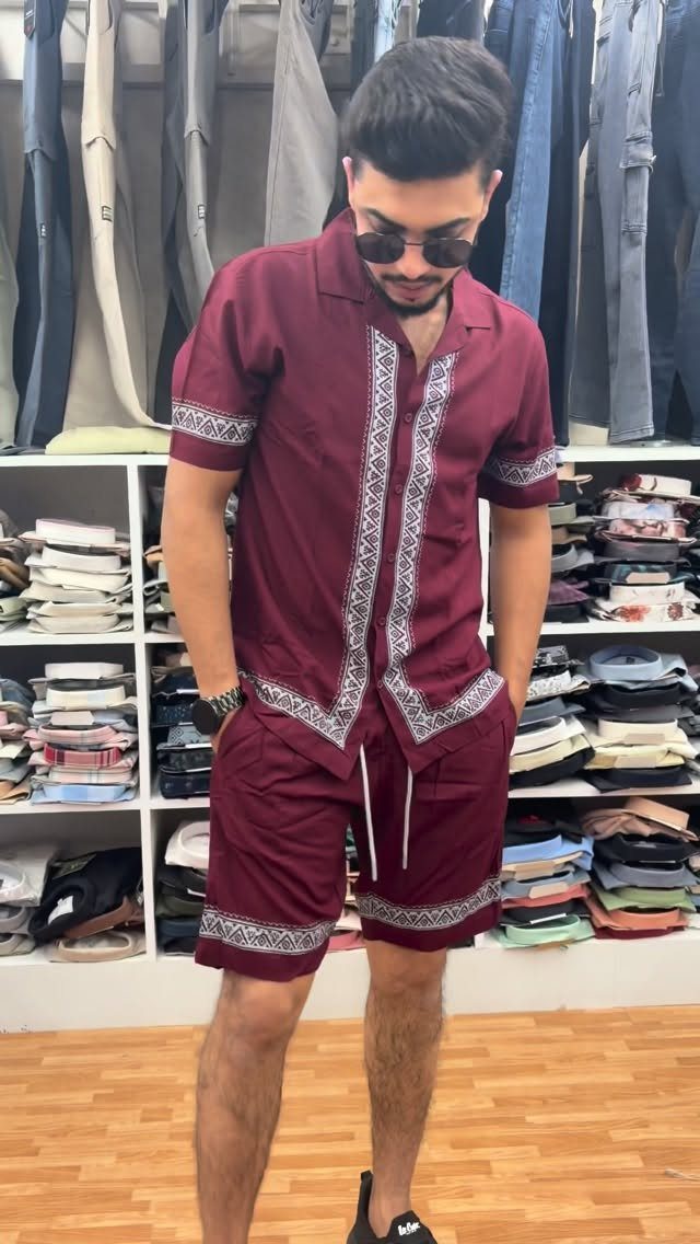 Man wearing a matching maroon embroidered short-sleeved shirt and shorts set in a store.