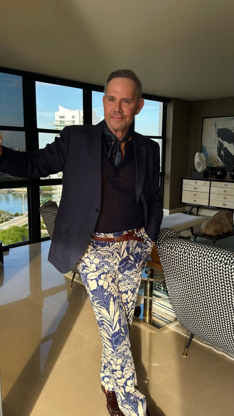 Man wearing a navy blazer and bold blue floral print trousers in a room.