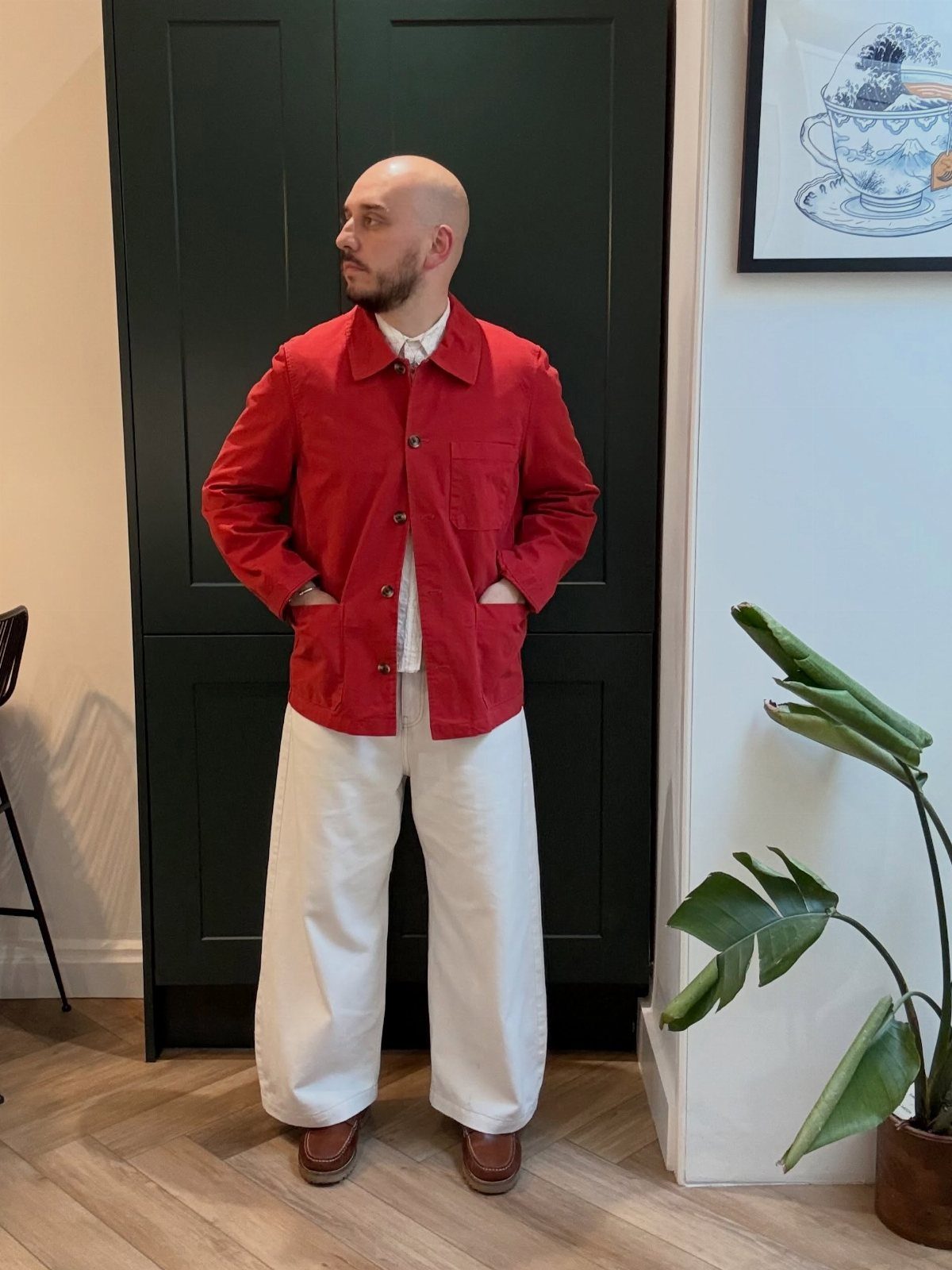 Man wearing a red jacket and wide white trousers standing in a room.