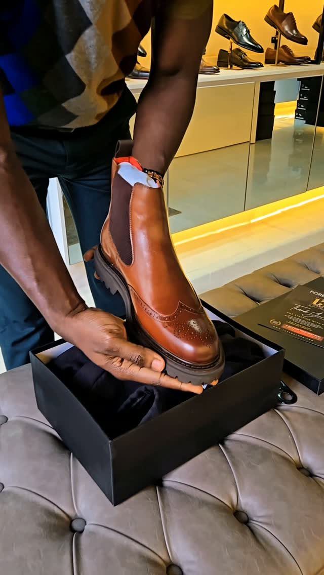 Brown leather brogue boot with decorative perforations resting on a black shoebox