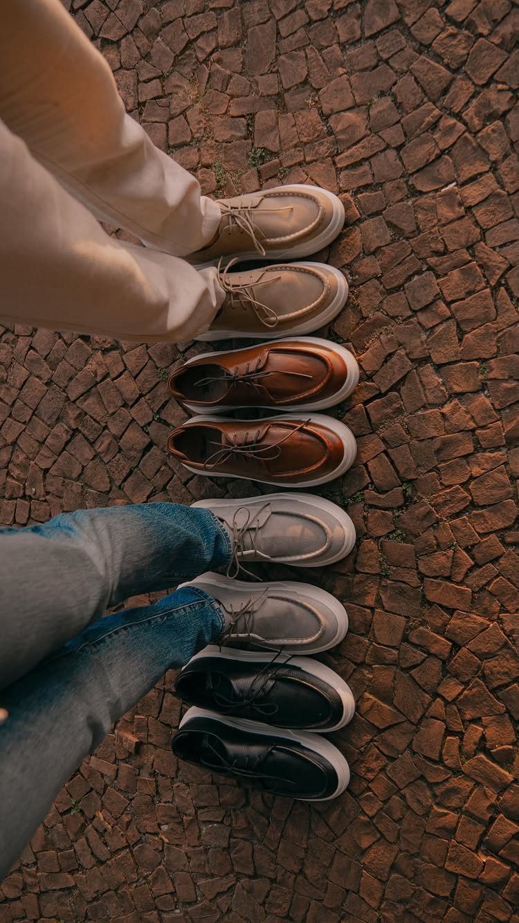 Four pairs of casual leather derby shoes in various colors on cobblestone pavement.