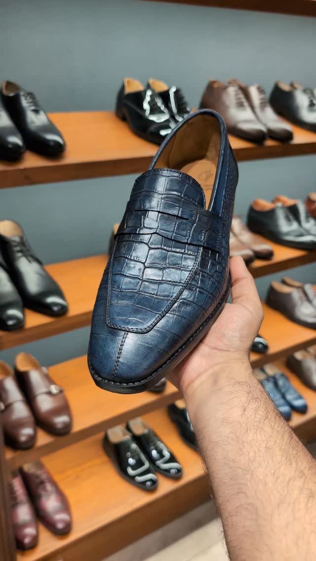 Navy blue crocodile-embossed leather loafer held up in a shoe store