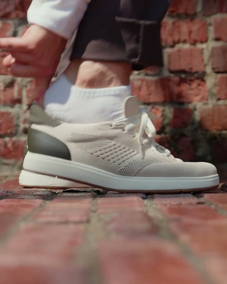 Cream lace-up sneaker with white sole and grey heel on red brick ground