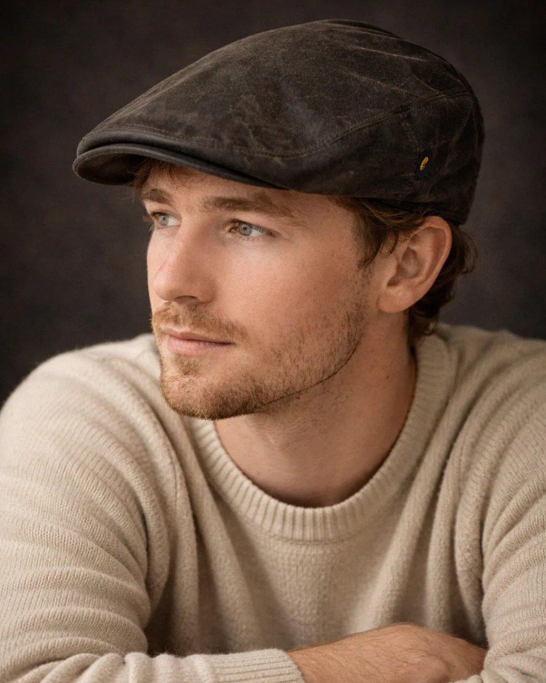 Man wearing a dark grey flat cap and a cream knit sweater.