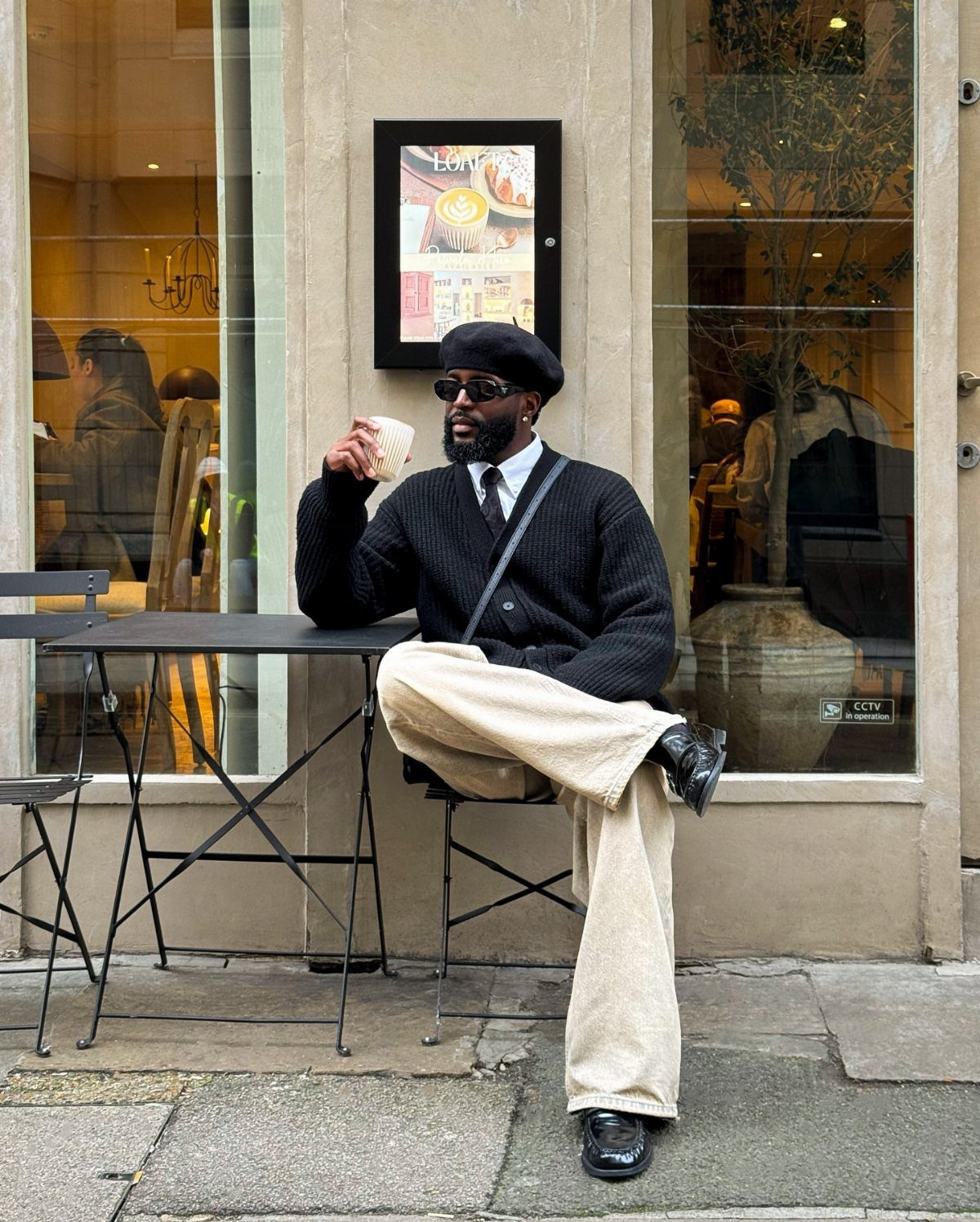 Man in black beret and beige corduroy pants sitting at outdoor cafe table