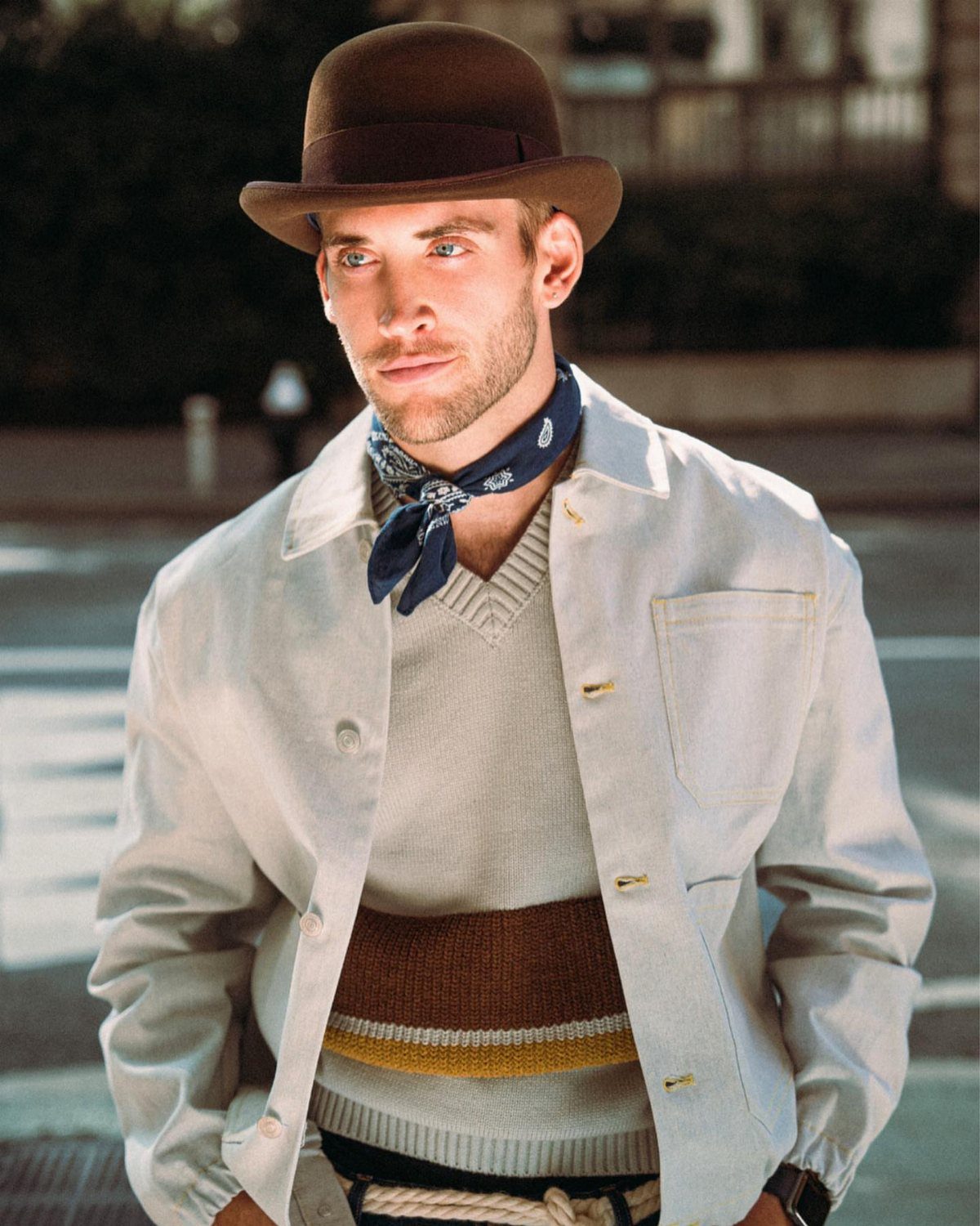 Man wearing a brown bowler hat, grey overshirt, and blue patterned neckerchief.