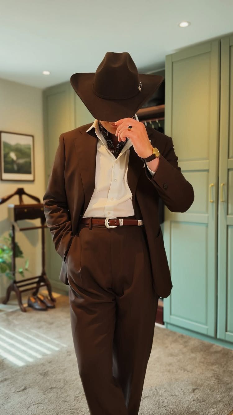 Man in a brown cowboy hat and matching brown suit standing indoors.