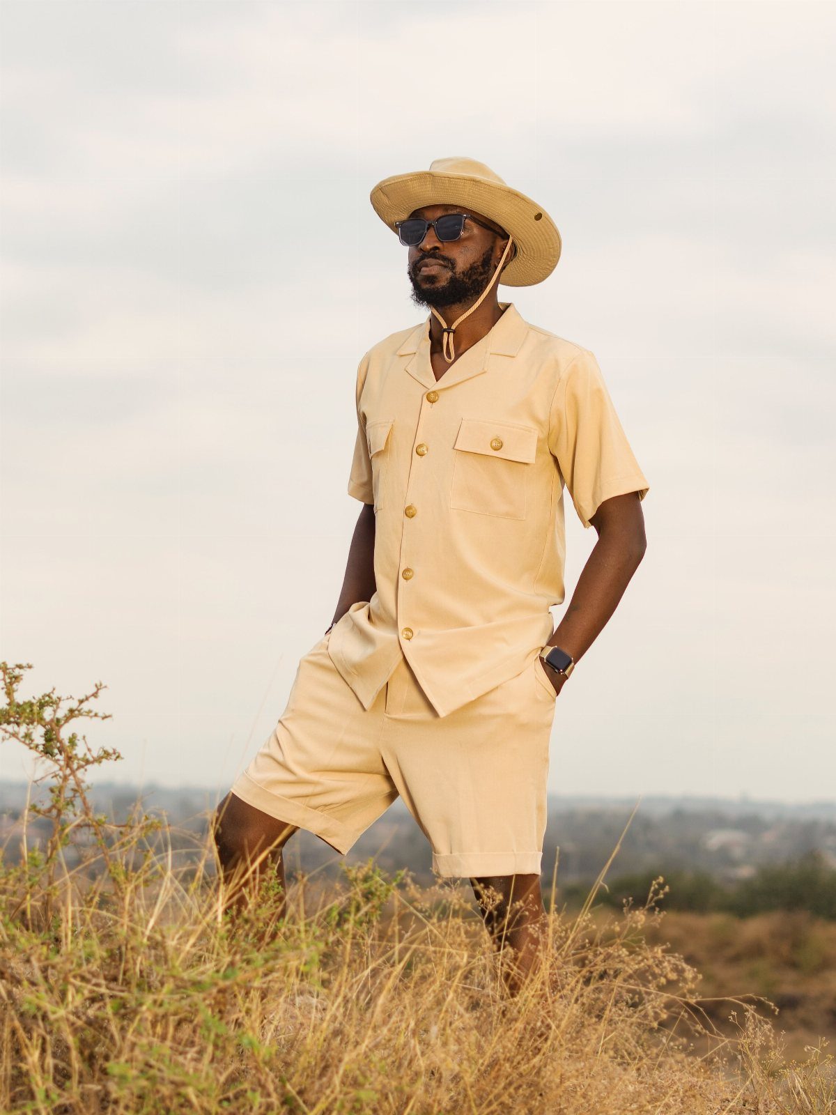Man in tan safari hat and matching outfit standing in a grassy field.