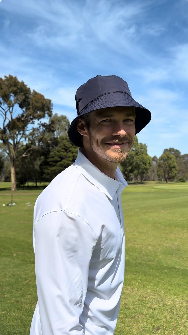 Man in a navy blue bucket hat and white shirt on a golf course.