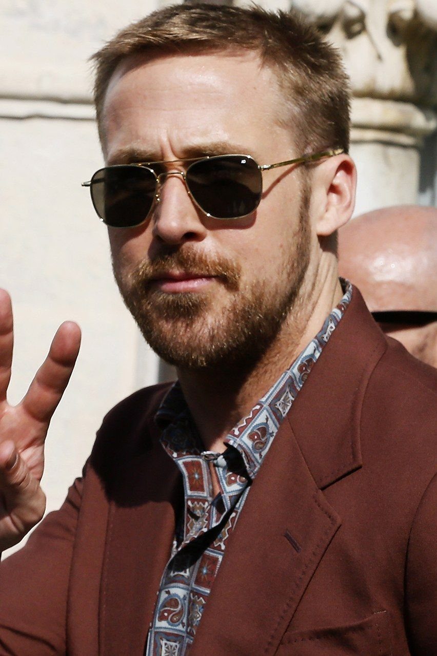 Man with beard wearing gold aviator sunglasses and a maroon blazer outdoors.