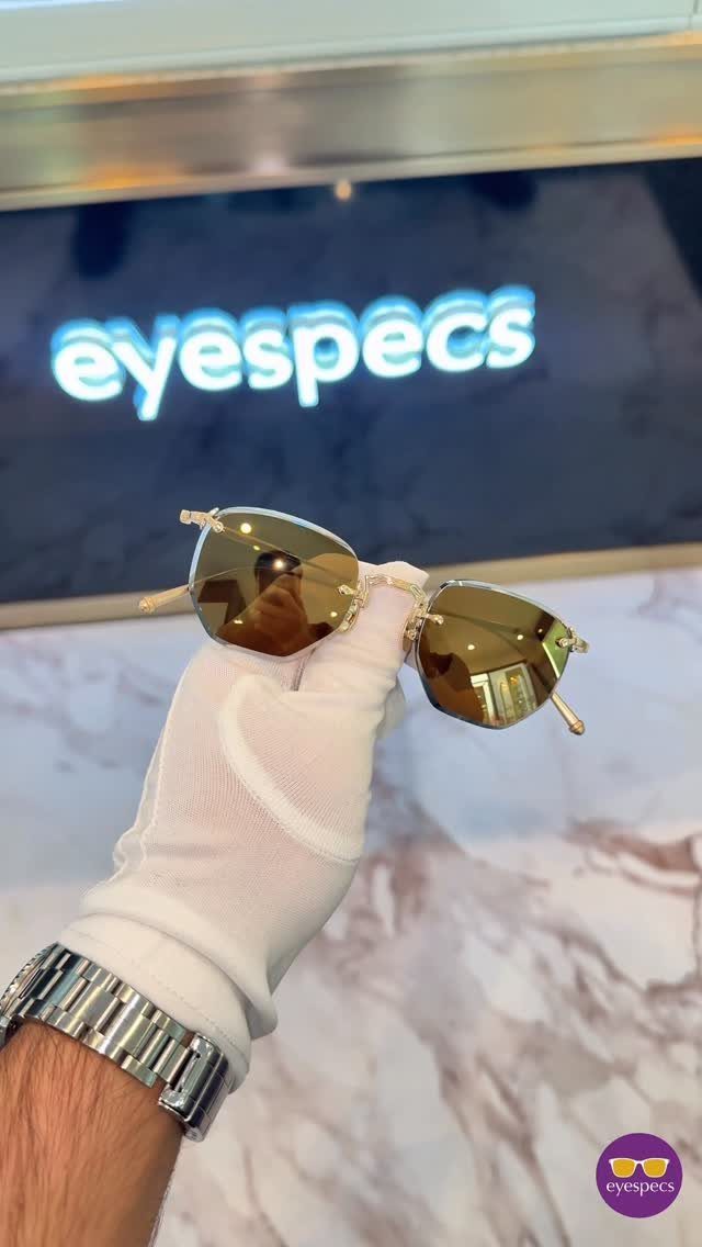 Gold-framed sunglasses held by a gloved hand against a marble background.