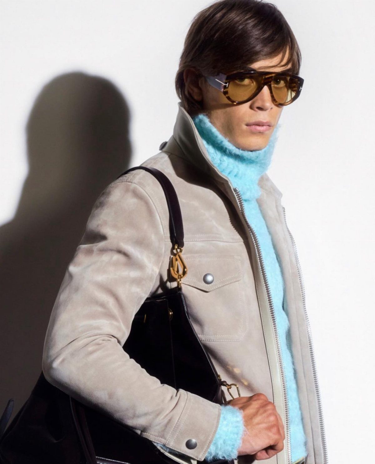 Man wearing oversized brown-tinted high fashion sunglasses and a beige suede jacket.