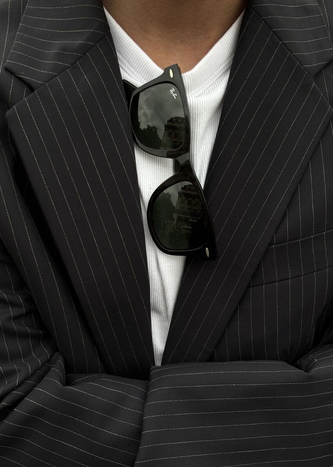 Black Wayfarer sunglasses tucked into a white t-shirt and black pinstriped blazer.
