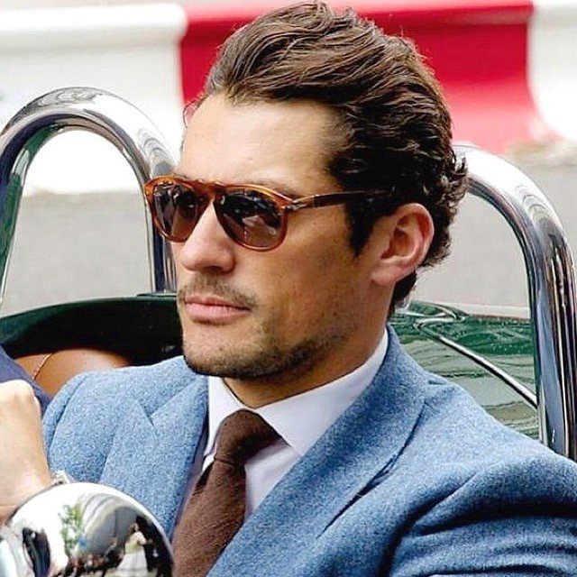 Man in a blue suit and brown tie wearing tortoiseshell sunglasses in a car.