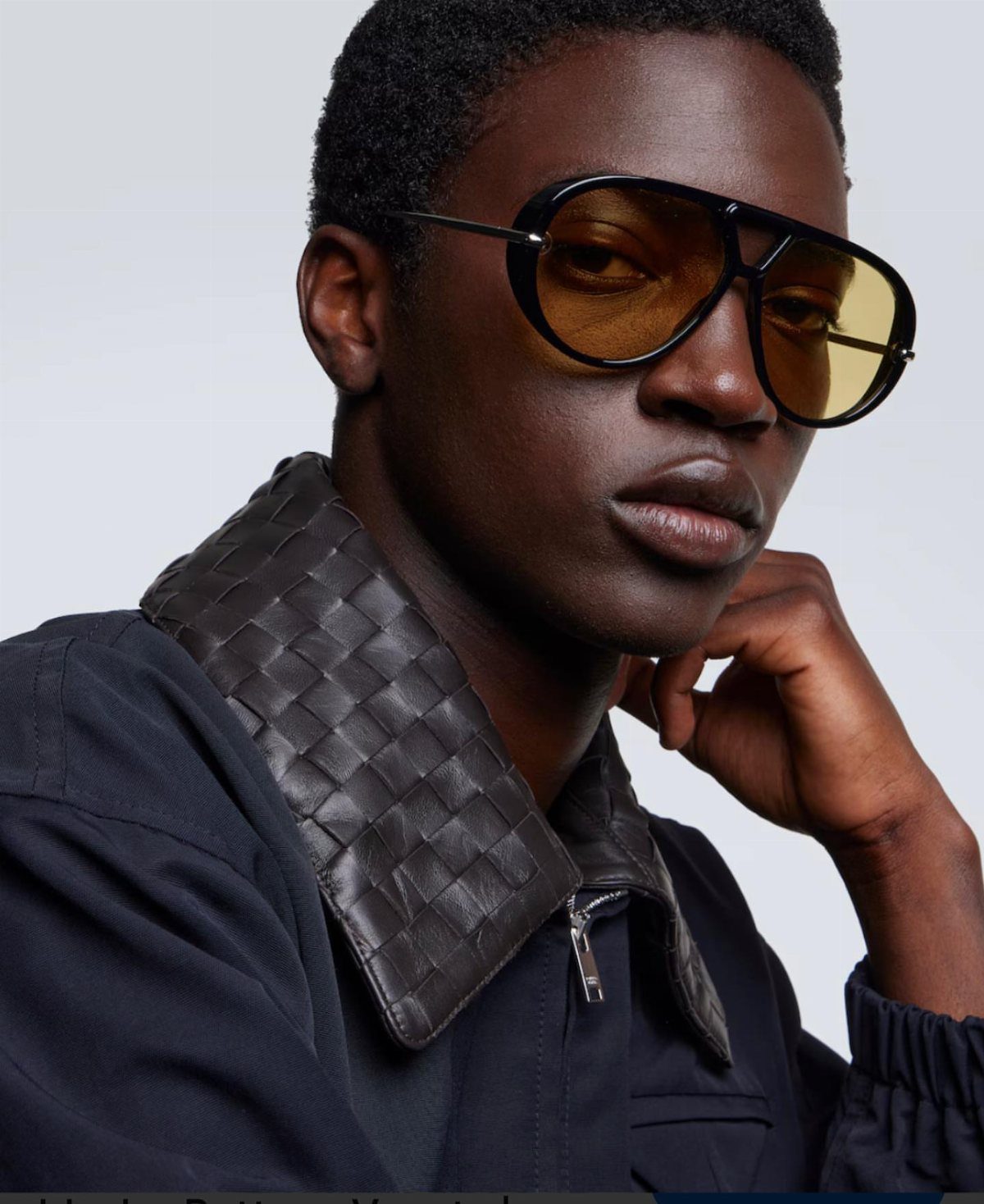 Man wearing oversized black high fashion sunglasses with yellow lenses and woven leather collar.