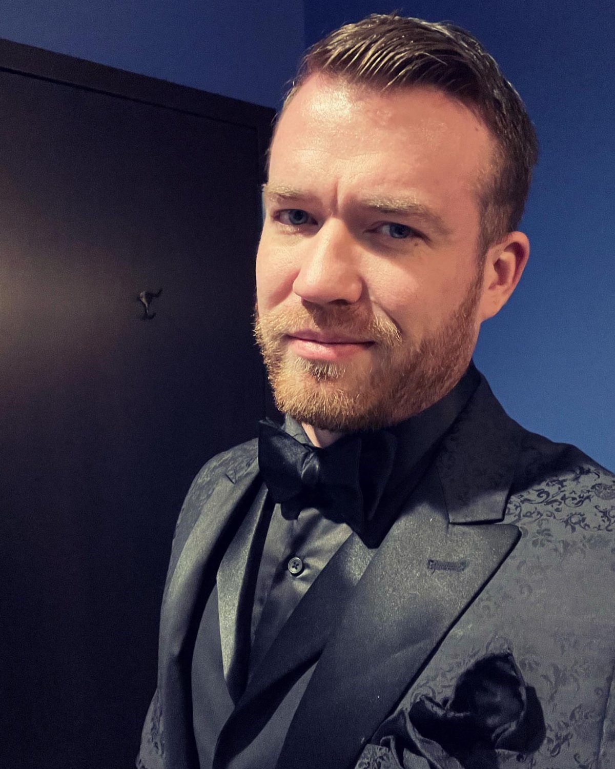 9 Men's Holiday Party Fashion Ideas That Actually Work 3 Man in a black patterned tuxedo with a bow tie posing for a portrait.