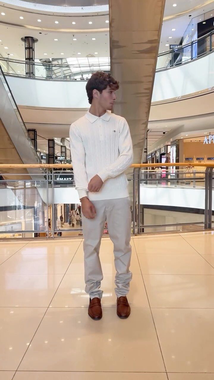 9 Men's Holiday Party Fashion Ideas That Actually Work 7 Man in white knit polo and grey trousers standing in a shopping mall.