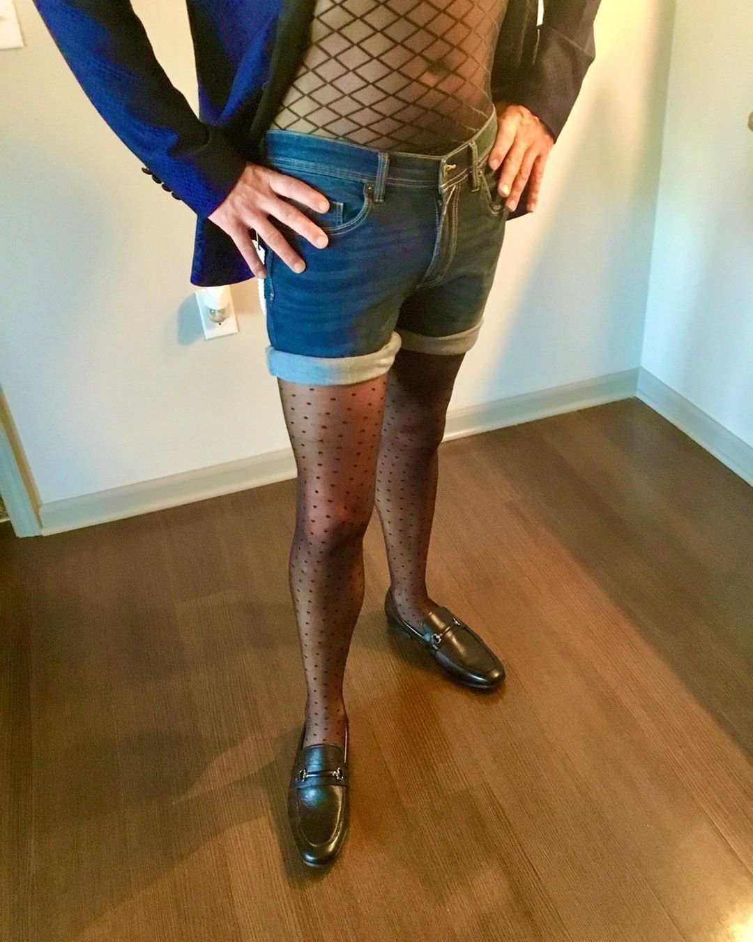 Person in blue blazer, denim shorts, and black polka-dot pantyhose with leather loafers.