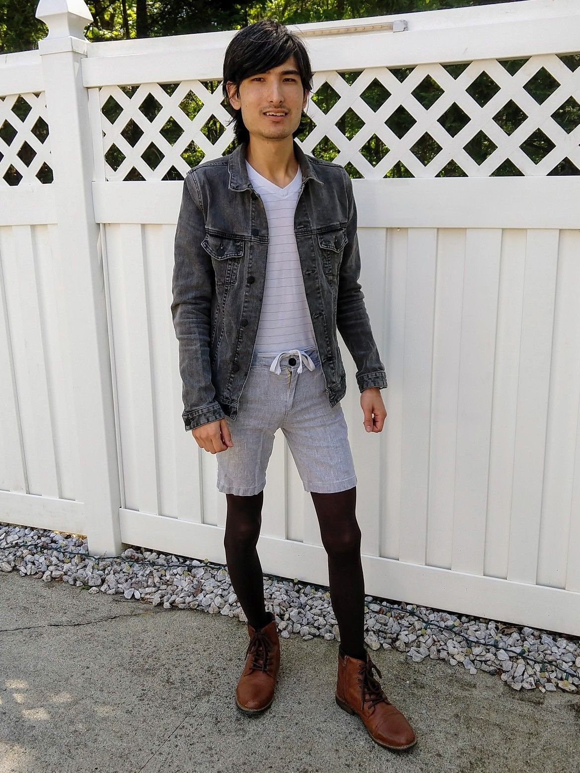 Man wearing grey denim jacket, light grey shorts, black tights, and brown boots.
