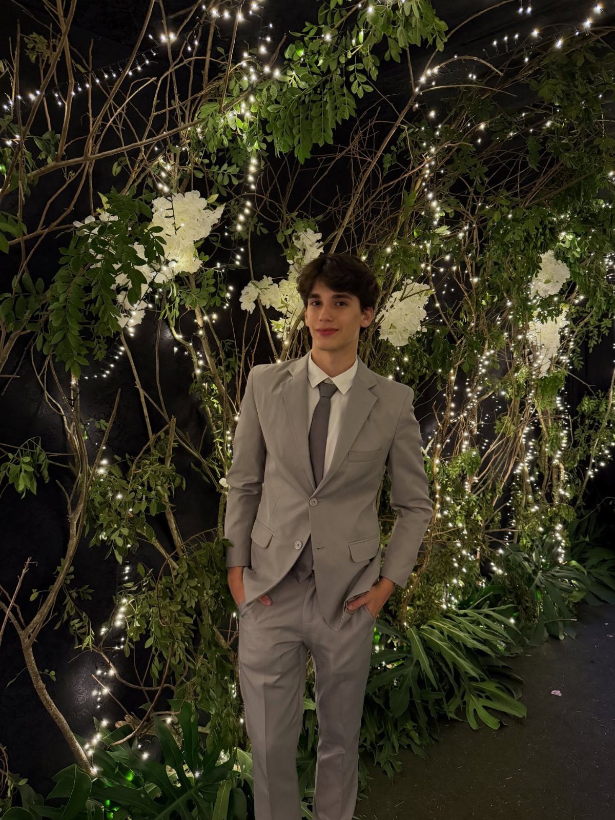 Young man in a slim-fit grey suit posing before a lit floral backdrop