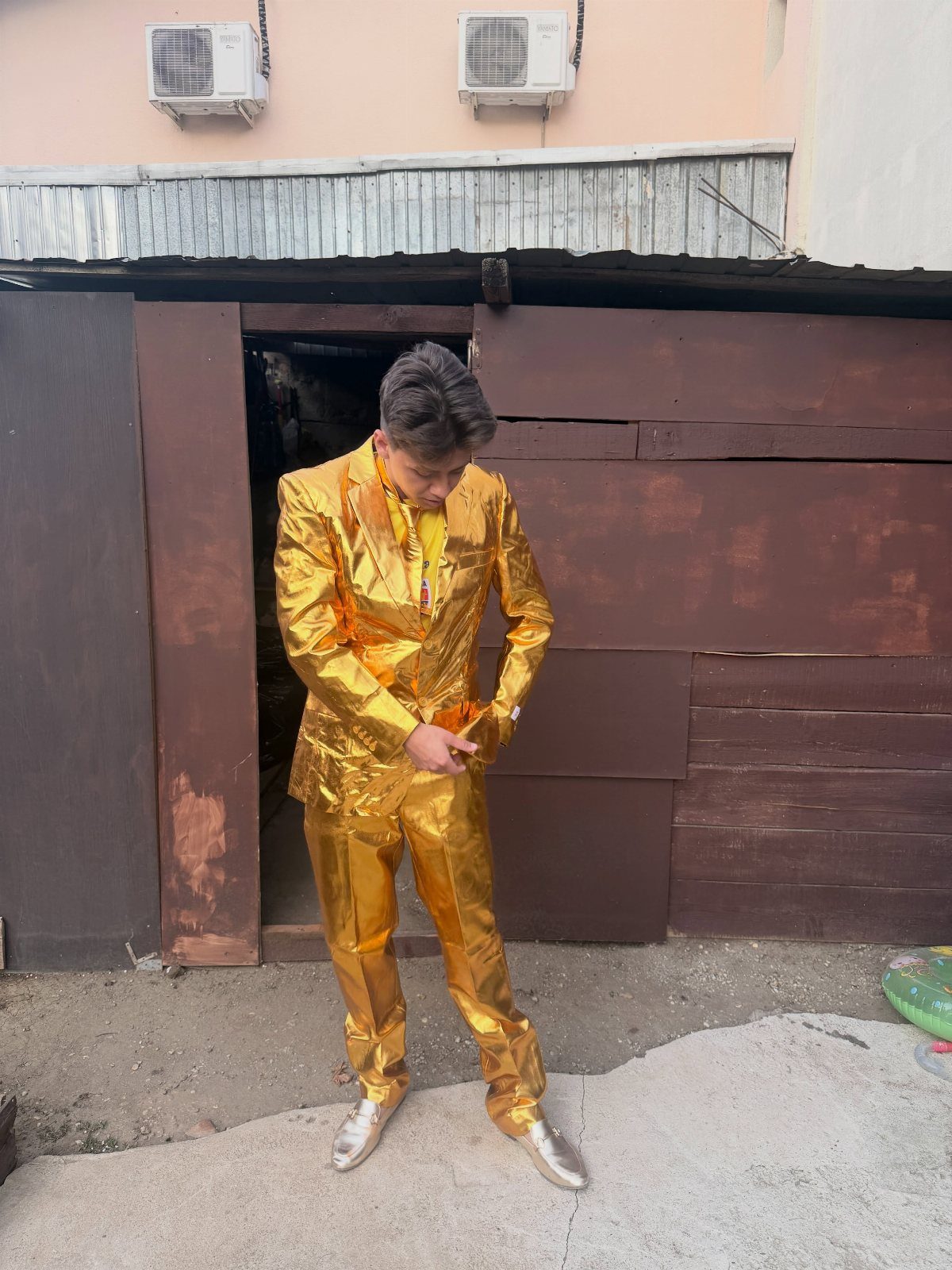 Man wearing a shiny metallic gold suit and gold shoes standing outdoors.
