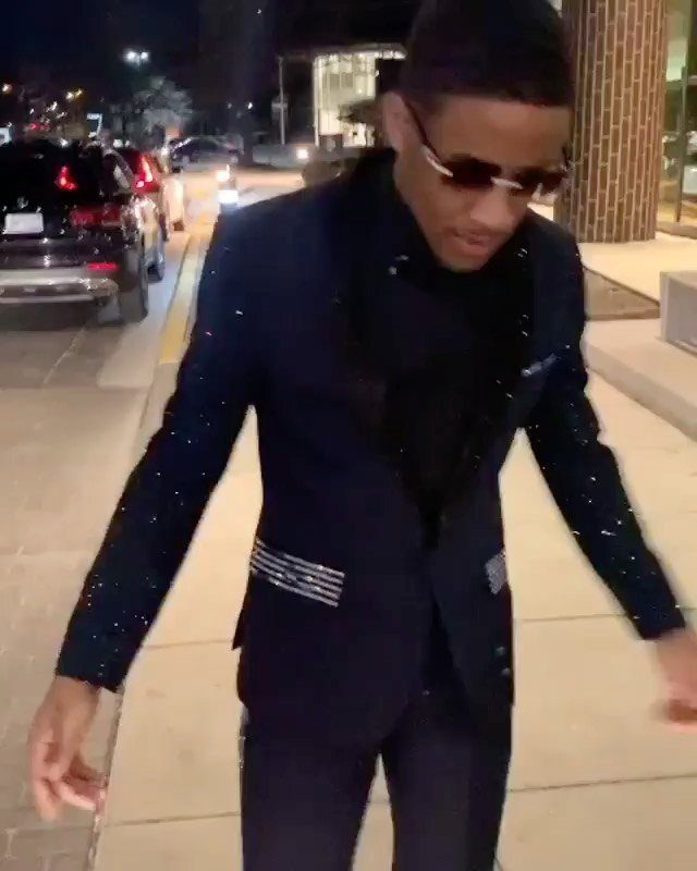 Young man in a sparkling navy blue blazer and sunglasses posing outdoors at night.