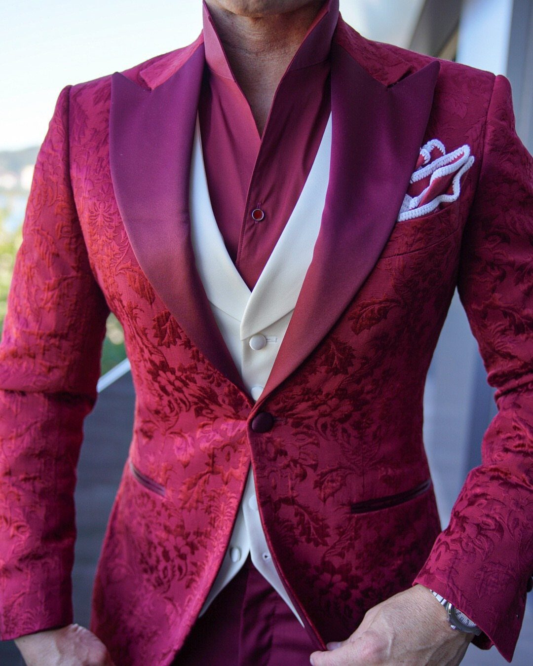 Man in a burgundy patterned suit with a cream waistcoat and white pocket square.