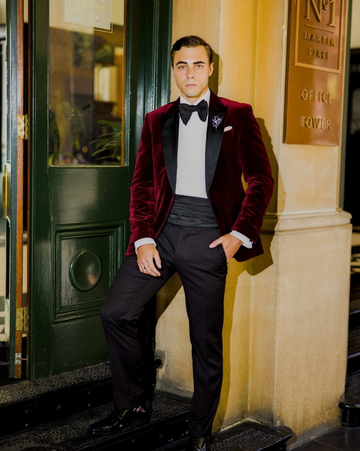 Man wearing a burgundy velvet dinner jacket with a black bow tie and trousers.