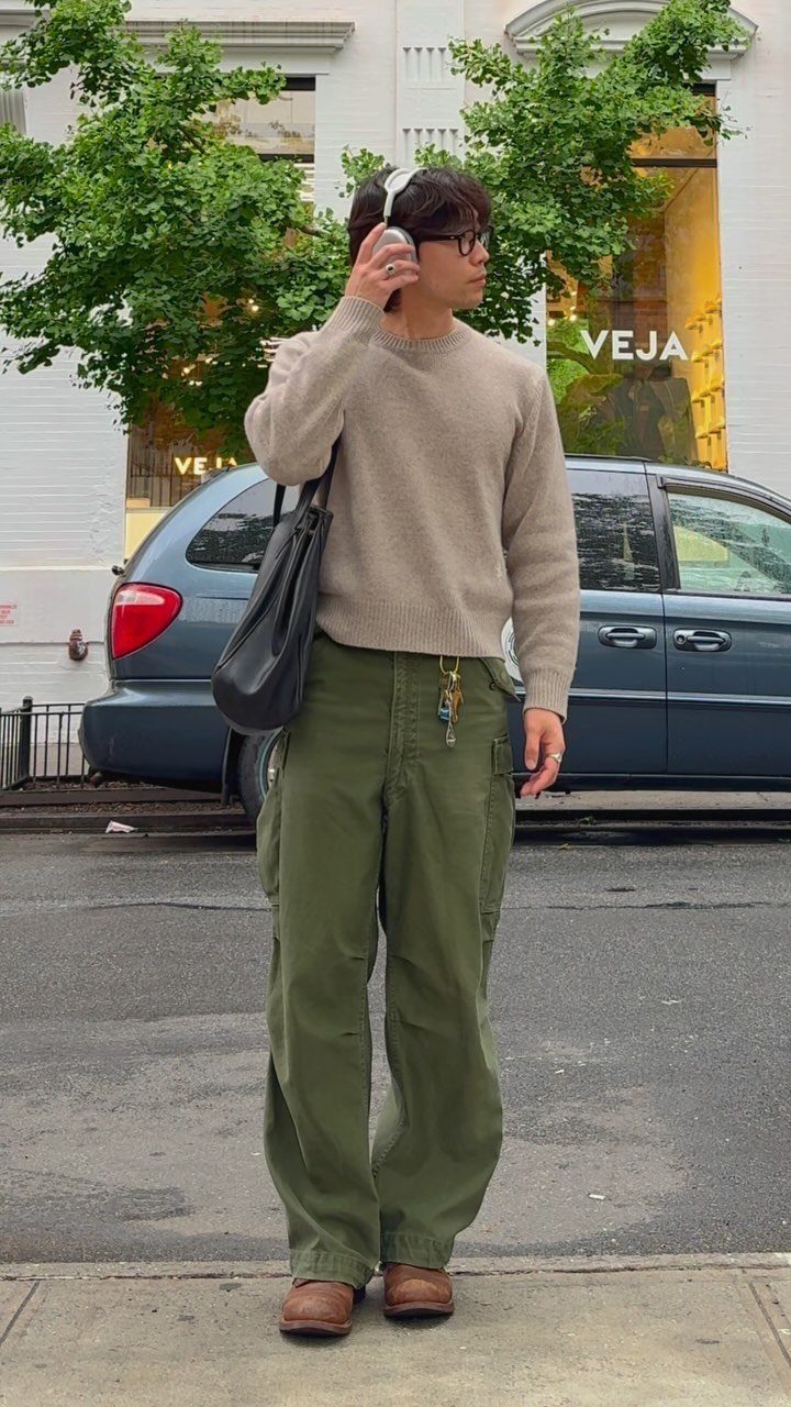 Man in beige sweater and olive cargo pants standing on a city street.