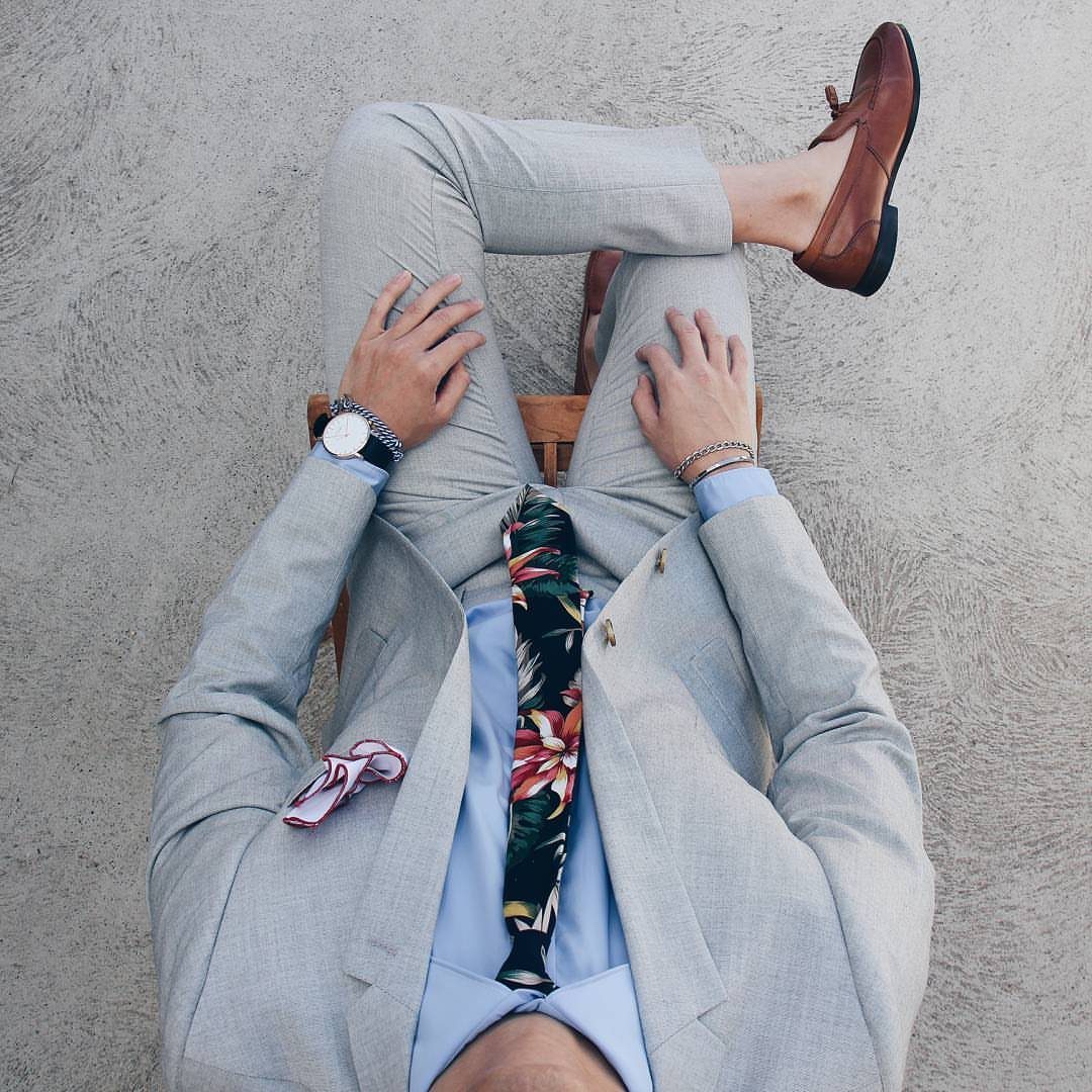 Man in a light grey suit with a floral tie and brown loafers.