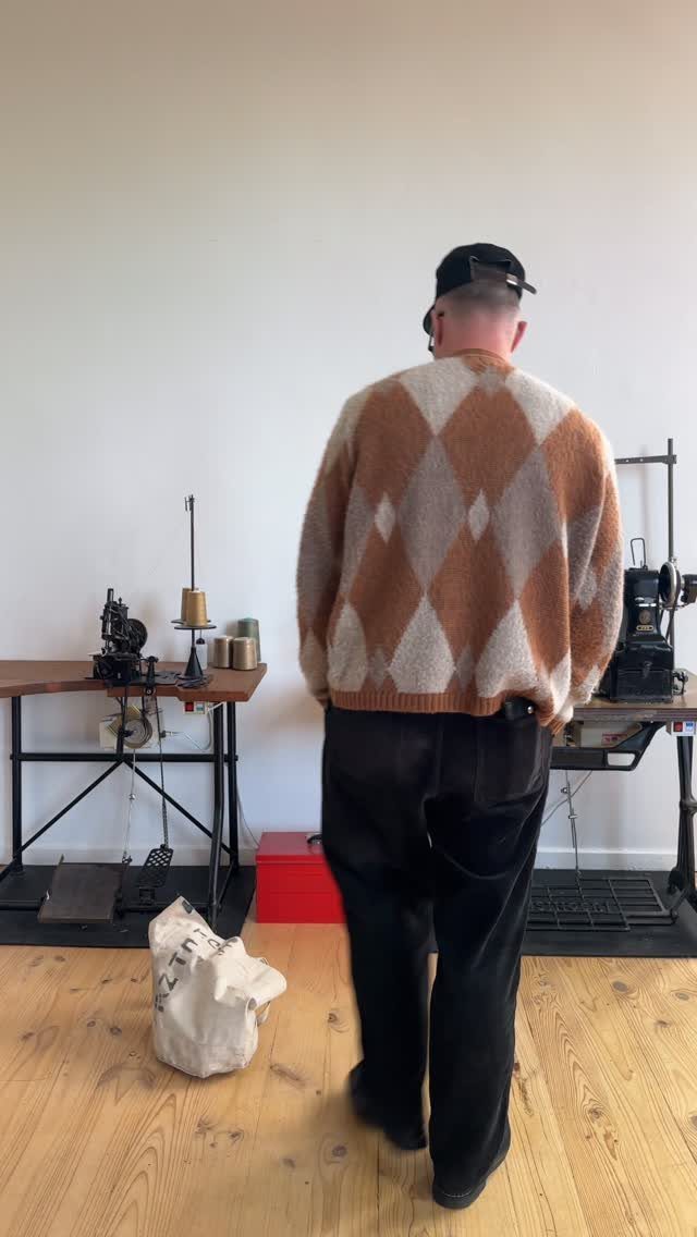 Man from behind wearing an argyle sweater and black trousers in a studio.