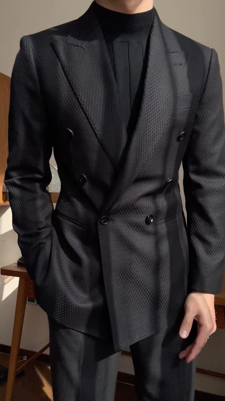 Man wearing a black textured double-breasted blazer and a black turtleneck sweater.