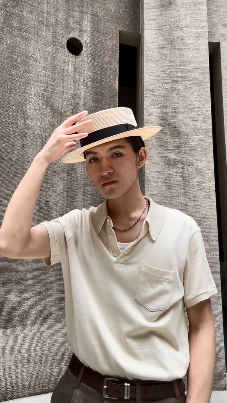 Man wearing a straw boater hat and cream polo shirt against a concrete wall