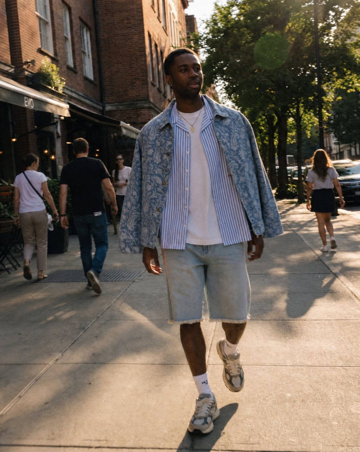 Man walking in a light blue patterned summer jacket and denim shorts.