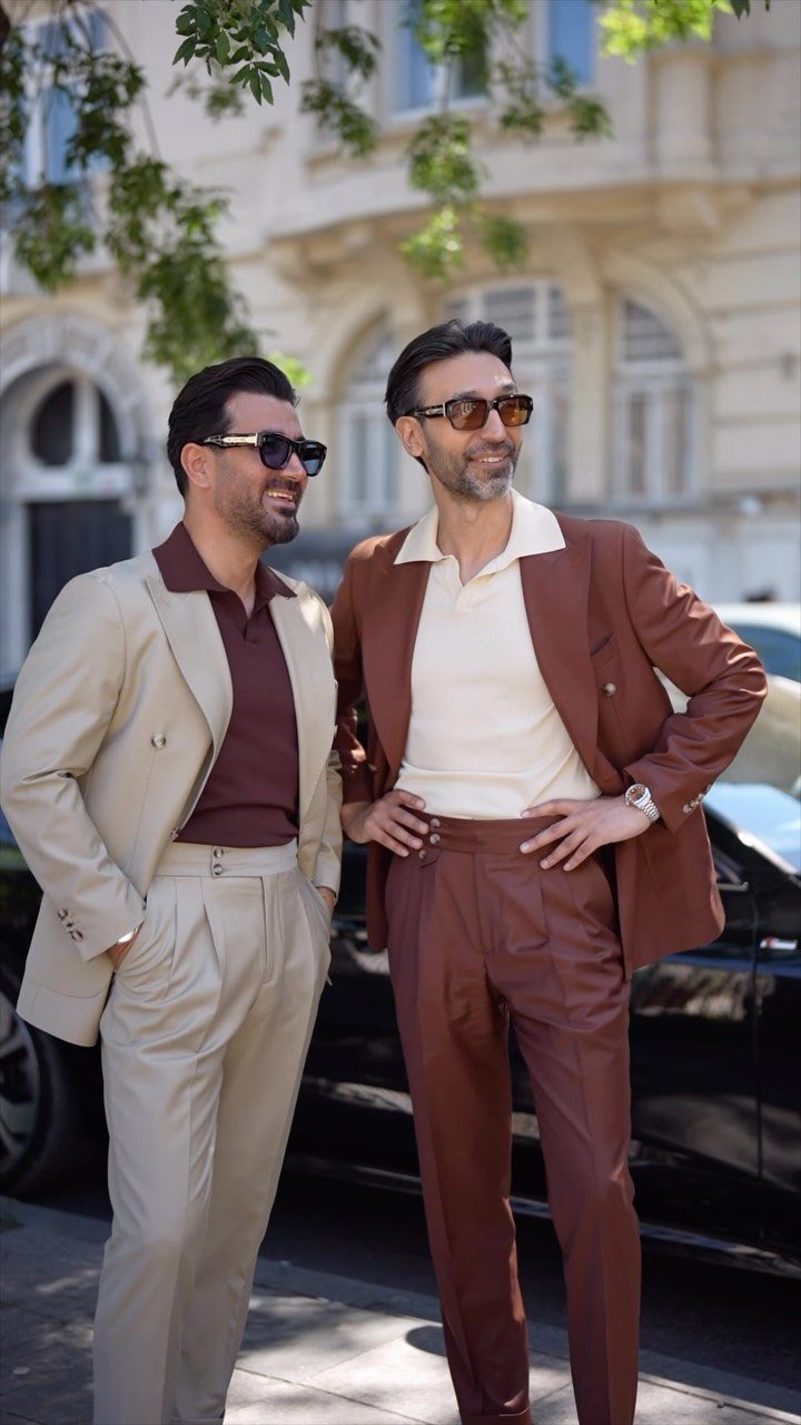 Two men wearing light-colored summer suits and sunglasses standing by a black car.