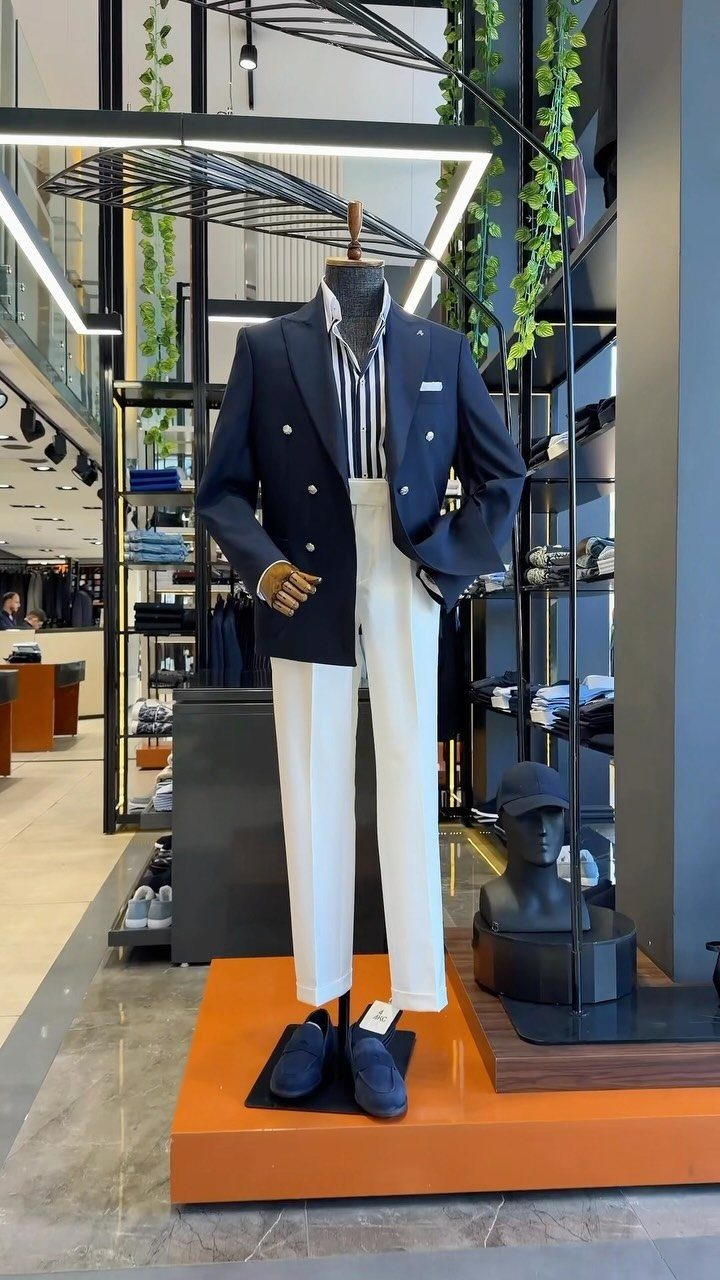 Mannequin wearing a navy double-breasted blazer, striped shirt, and white trousers in a store.