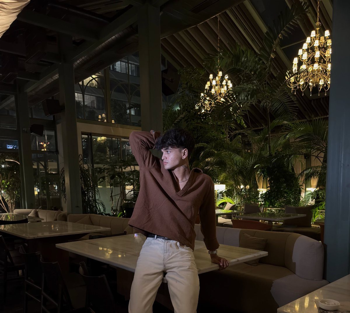 Man in brown v-neck sweater and white trousers posing in a restaurant