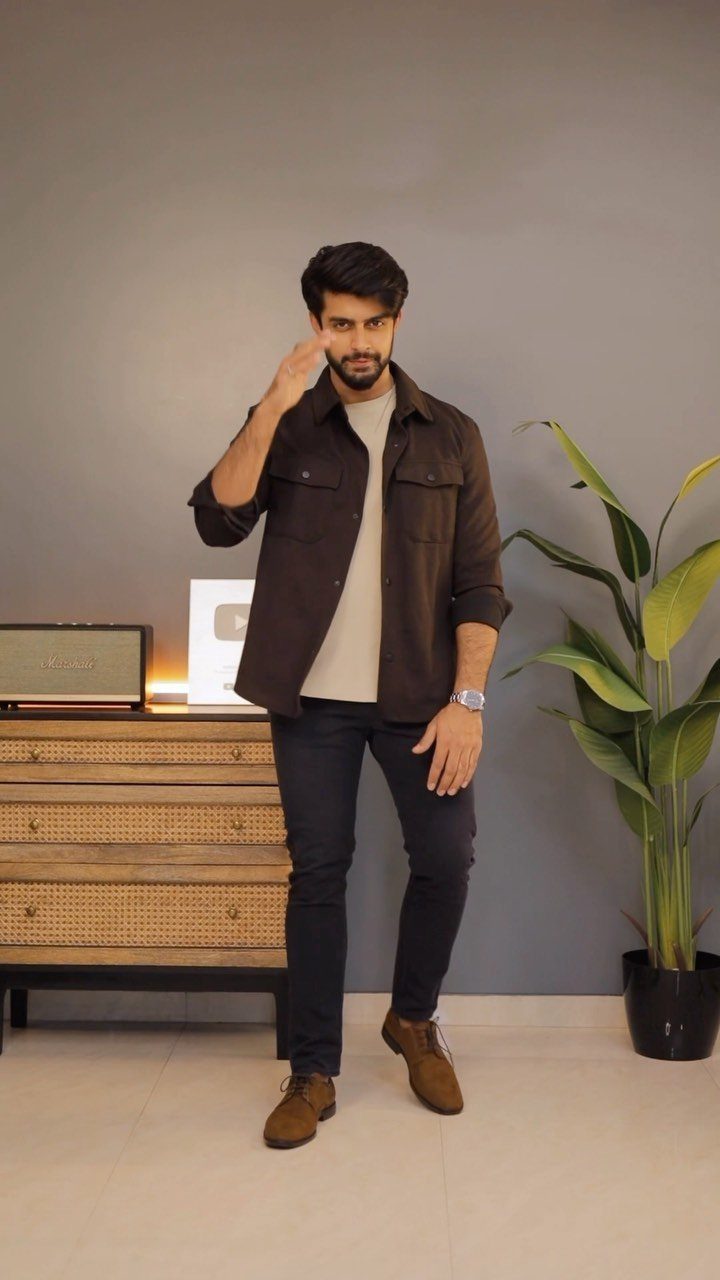 Man wearing a brown overshirt, beige t-shirt, dark trousers, and brown suede shoes.