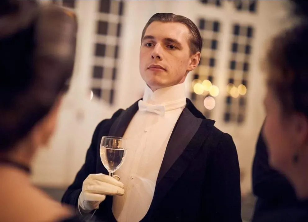 Man in black Victorian formal tailcoat and white bow tie holding a glass.