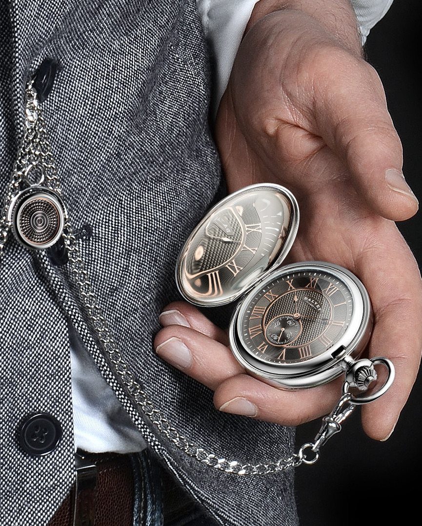 Man in grey waistcoat holding an open silver vintage pocket watch with chain.