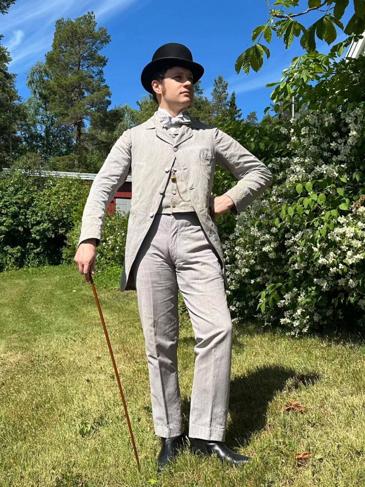 Man in light grey Victorian three-piece suit and bowler hat holding a cane.