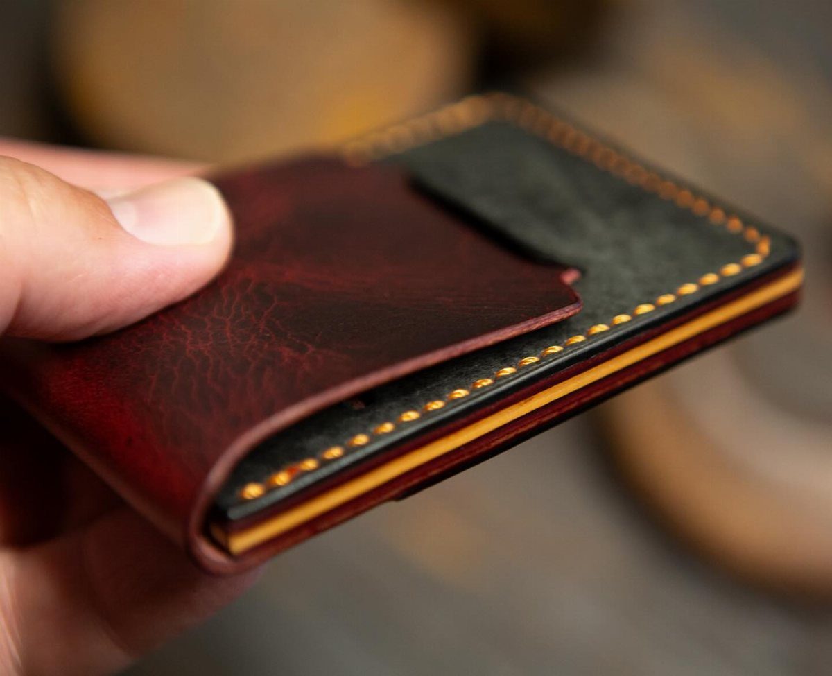 Slim bifold leather wallet in red and black with yellow stitching held by hand.