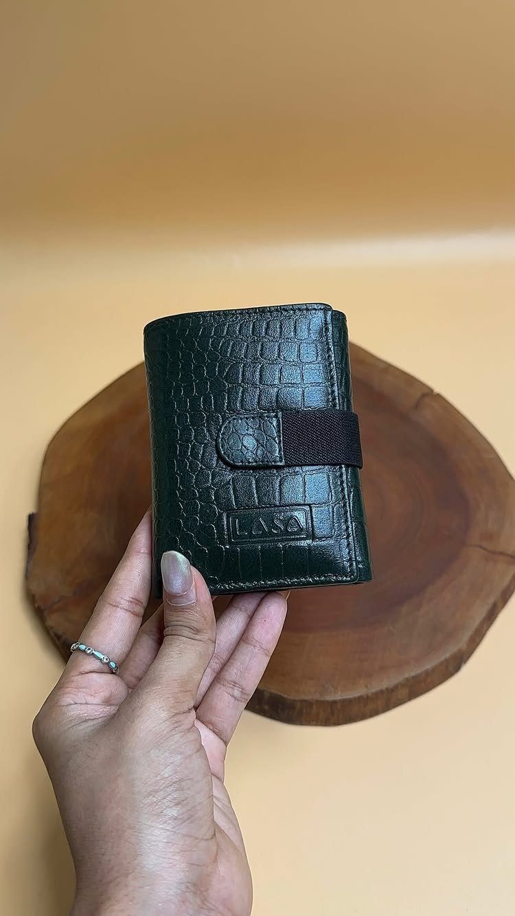 Dark green crocodile leather bifold wallet held by a hand over a wooden slice.