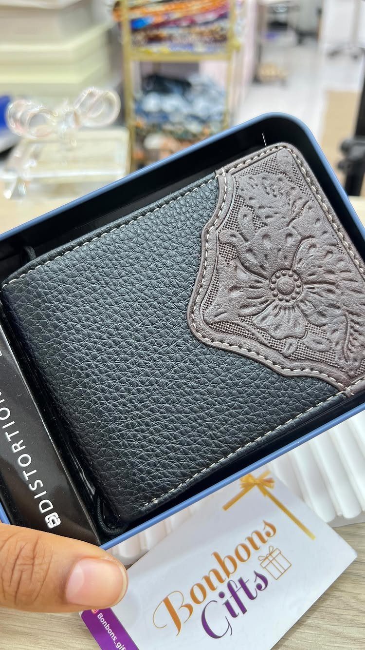 Black leather bifold wallet with embossed floral detail inside a blue gift box.