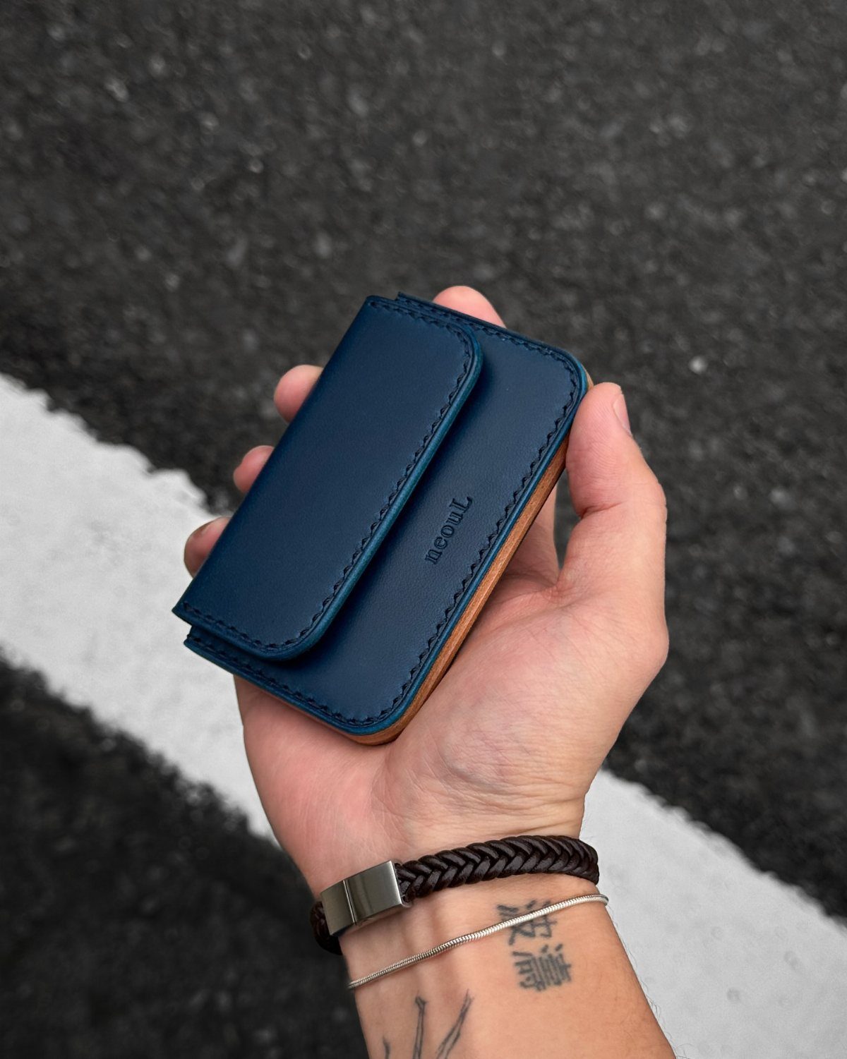 Navy blue leather bifold wallet held in a hand over asphalt road