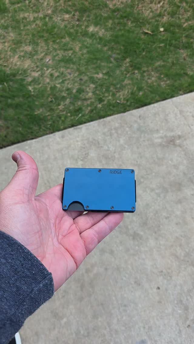 Blue metal Ridge wallet held in a person's hand outdoors on concrete.