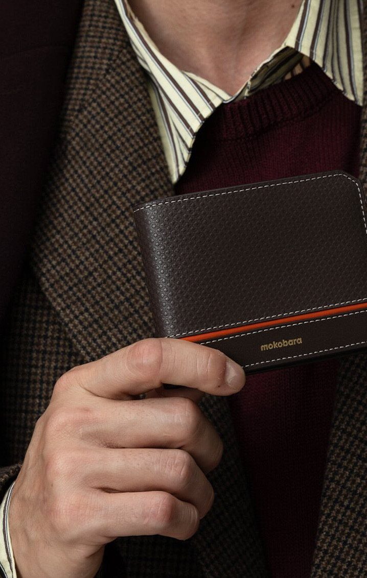 Dark brown leather bifold wallet with orange accent held by a man.