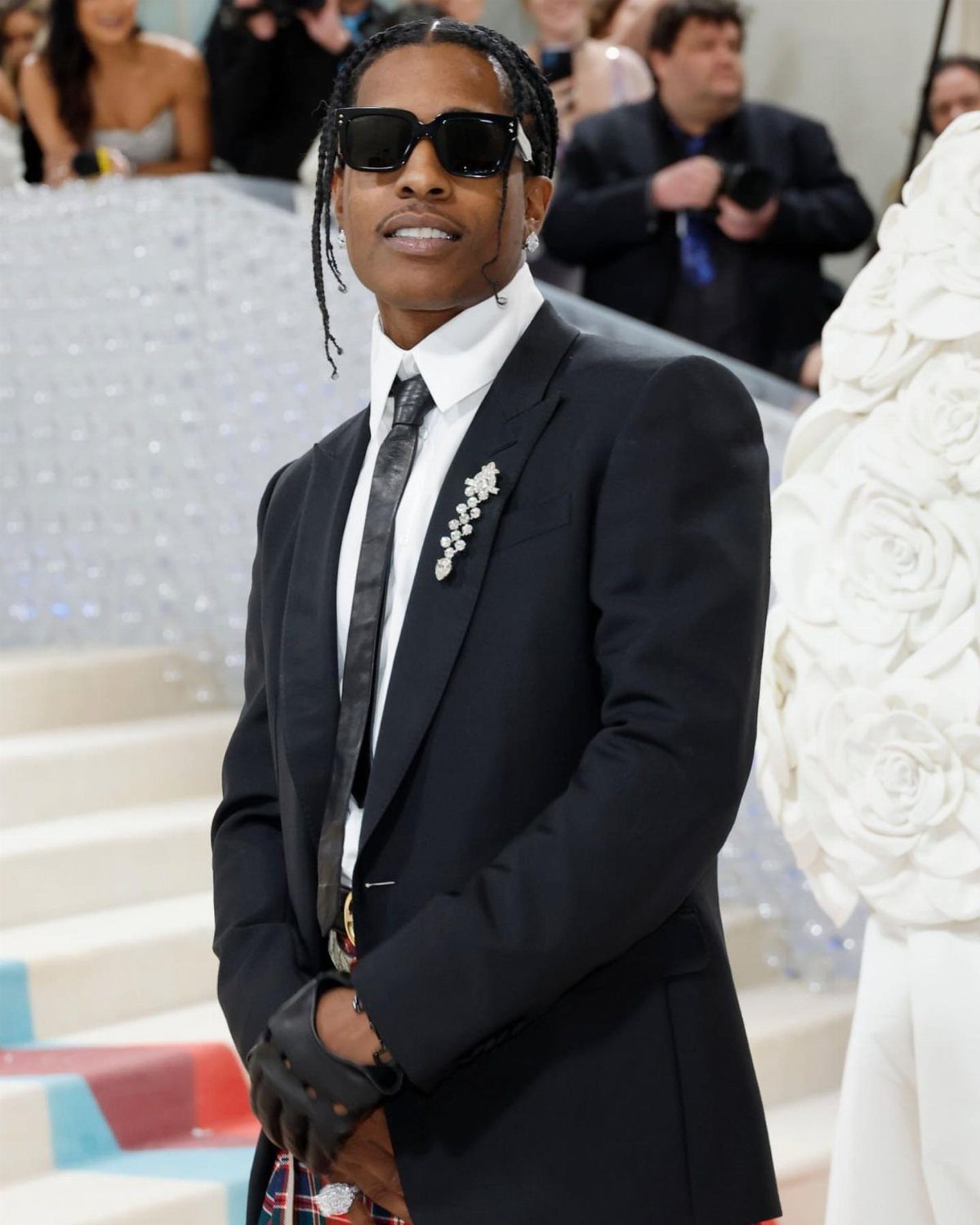 Man in black suit and sunglasses posing on white stairs at Met Gala.